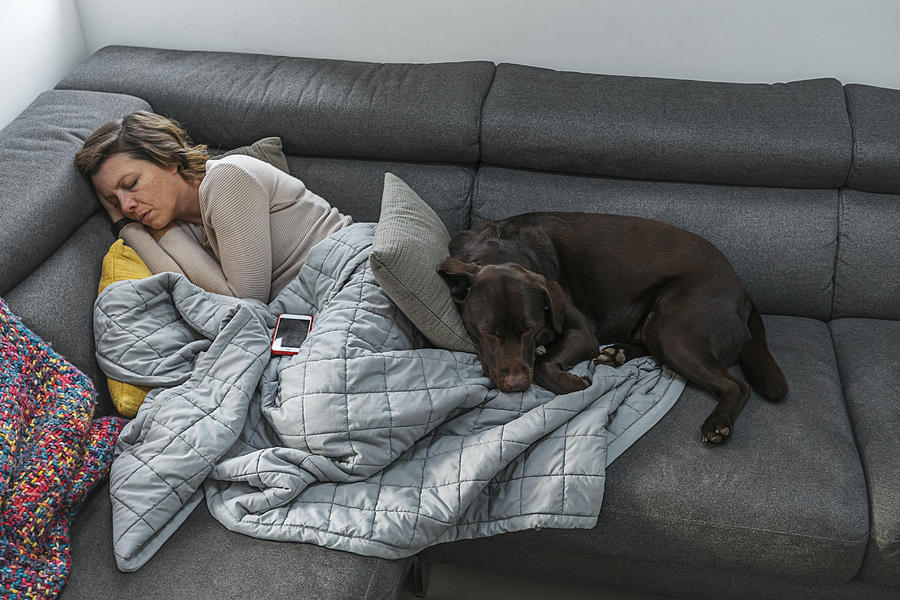 Woman asleep on sofa with pet dog Photograph by Justin Paget
