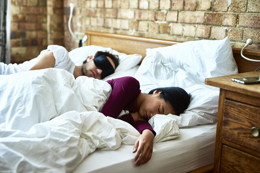 Woman asleep with hand on mattress and man wearing eye mask Photograph by 10000 Hours