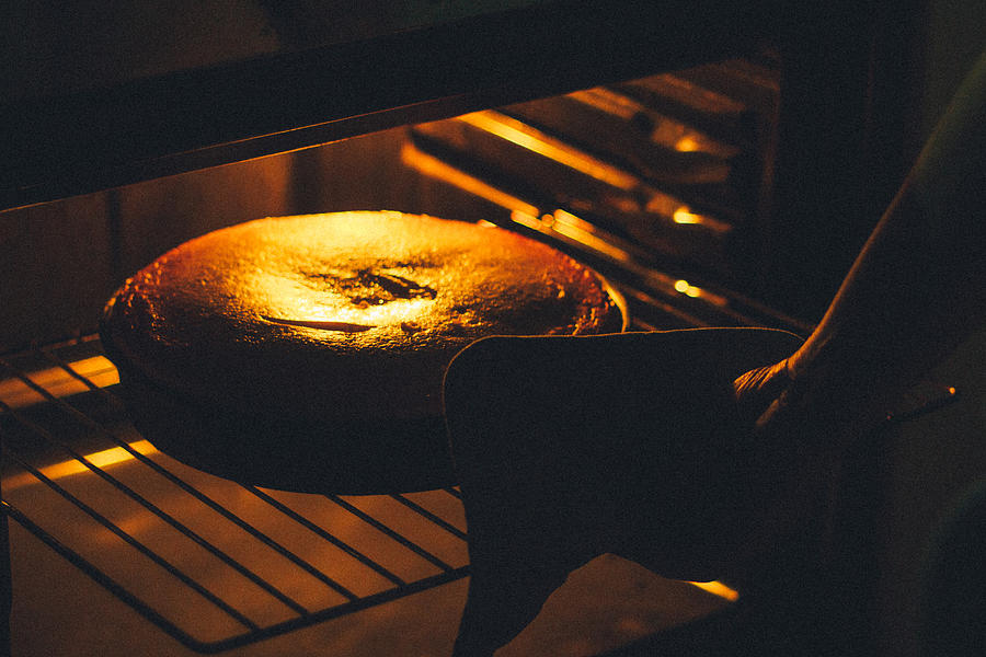 Woman baking cake in oven Photograph by Yompyz
