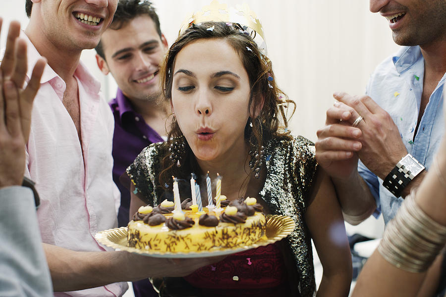 Woman blowing out candles on birthday cake Photograph by Floresco Productions