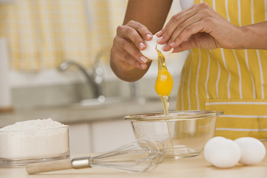 Woman breaking egg into bowl Photograph by Comstock Images