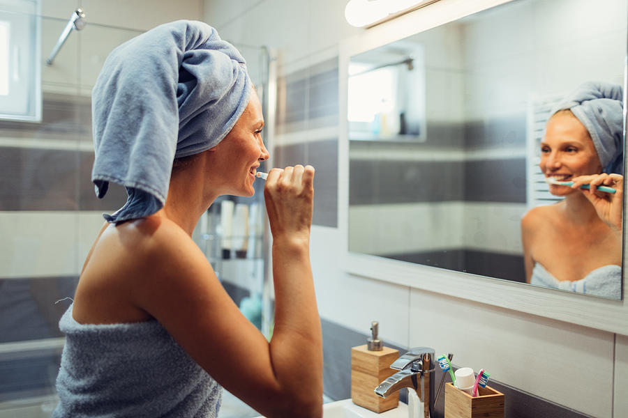 Woman brushing teeth in bathroom Photograph by Vgajic