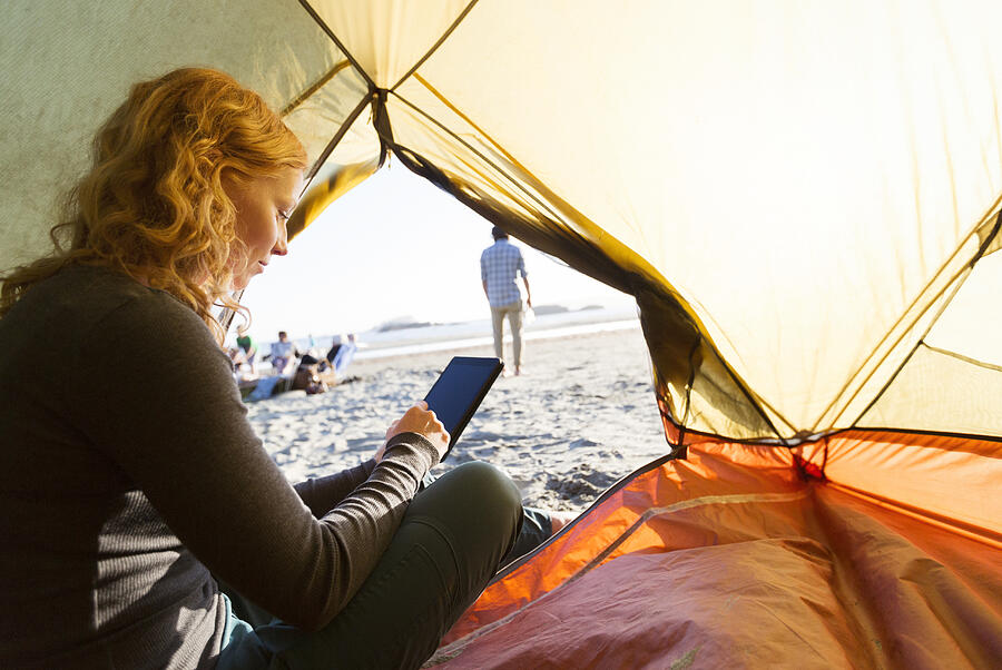 Woman camping using smart phone on beach at sunset Photograph by Compassionate Eye Foundation/Steven Errico