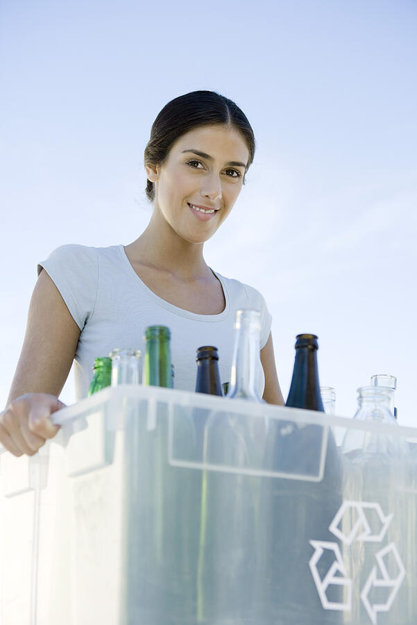Woman carrying recycling bin filled with glass bottles, smiling at camera Photograph by PhotoAlto/Sigrid Olsson