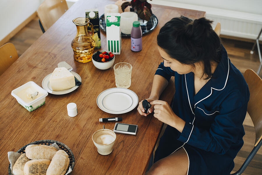 Woman checking diabetes while having breakfast on table at home Photograph by Maskot