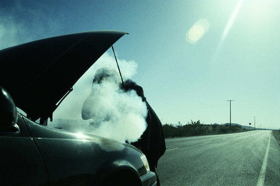 Woman checking smoking hood of car Photograph by Paul Taylor
