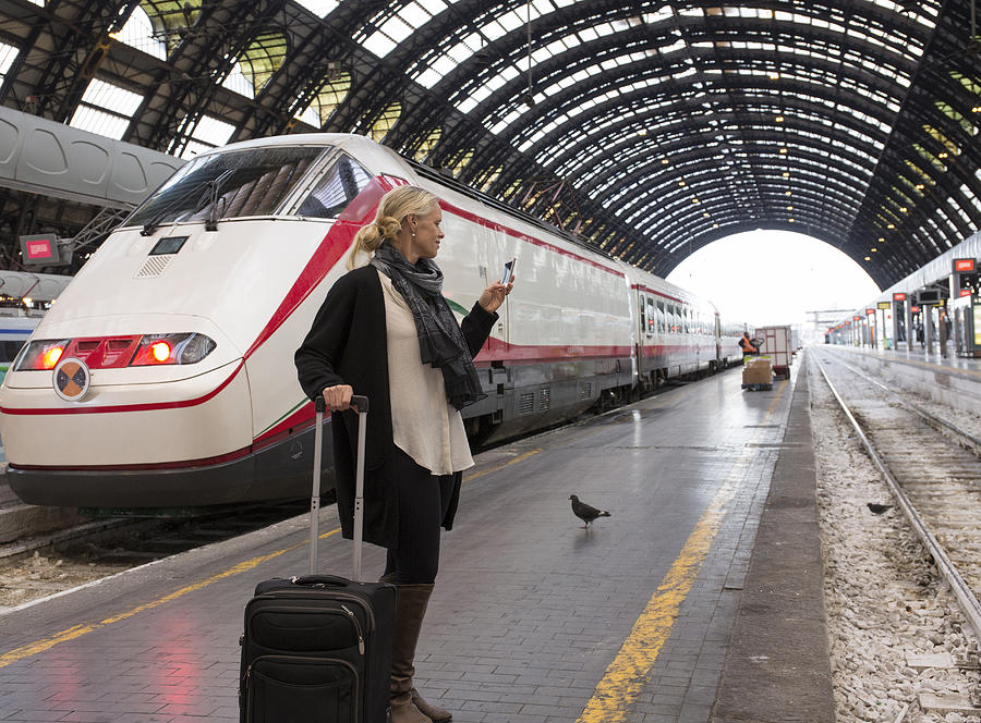 Woman checks timetable on phone, train platform Photograph by Ascent/PKS Media Inc.