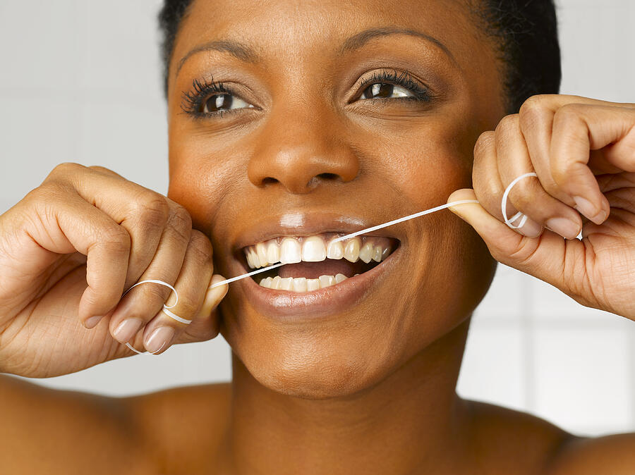 Woman cleaning teeth with dental floss, close up, studio shot Photograph by Peter Dazeley