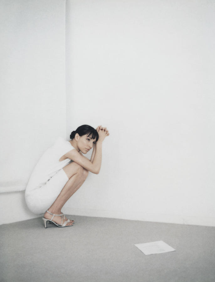 Woman crouching in corner of room, piece of paper on floor Photograph by Matthieu Spohn