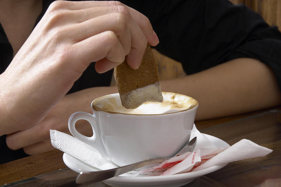 Woman dipping bisuit into coffee, close-up Photograph by RPMG srl