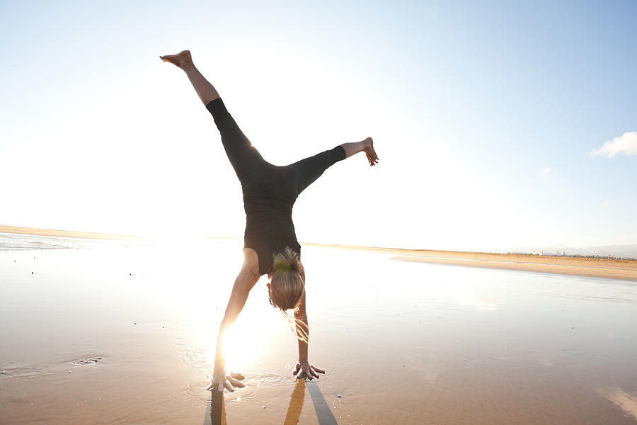 Woman Doing A Cartwheel On The Beach Photograph by Amriphoto