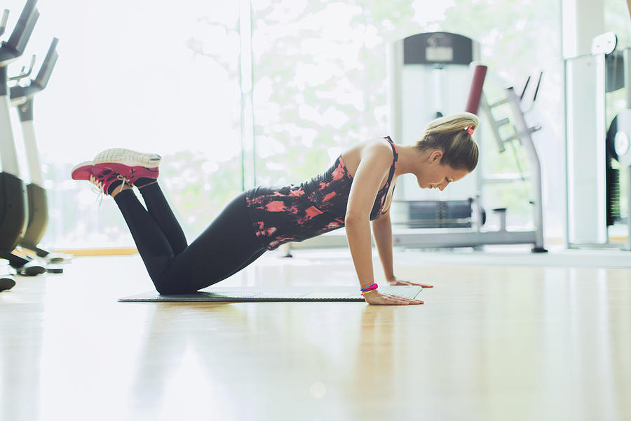 Woman doing push-ups on knees at gym Photograph by Caia Image