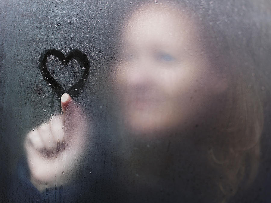 Woman drawing a heart on window on a rainy day. Photograph by David Trood