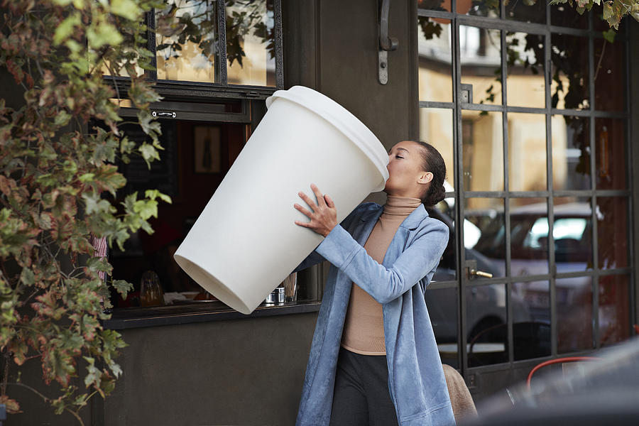 Woman drinking coffee from large disposable cup at take away counter of cafe Photograph by Klaus Vedfelt
