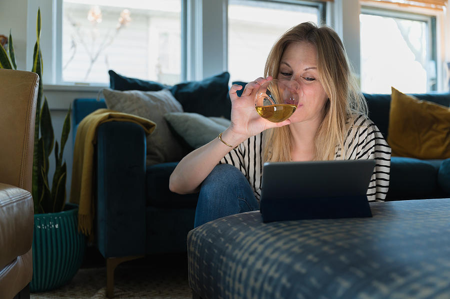 Woman drinking wine and looking at tablet at home Photograph by Jamie Grill