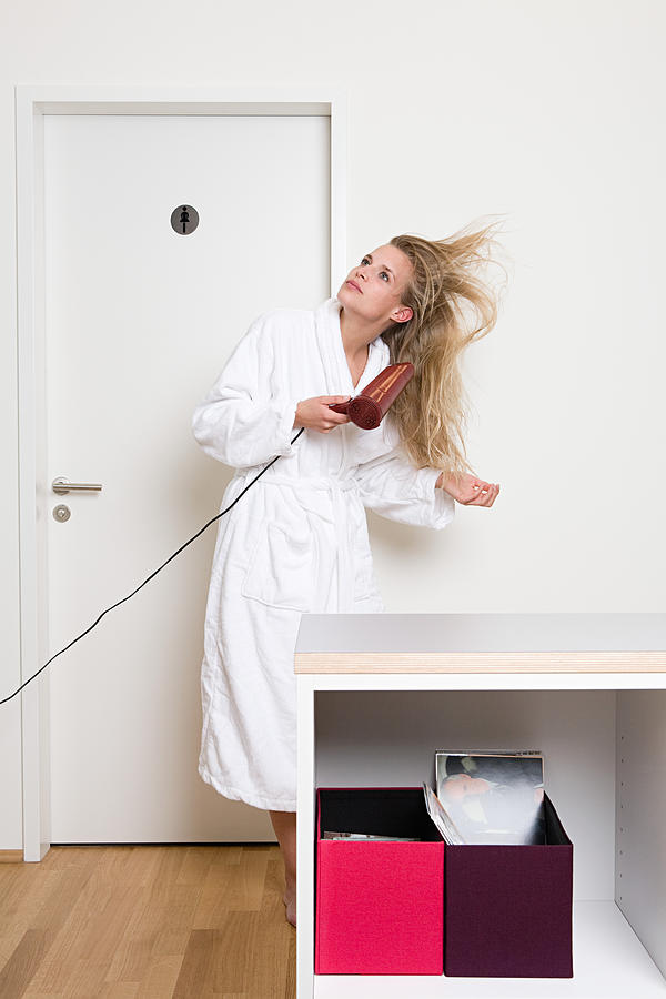 Woman drying her hair in office Photograph by Image Source