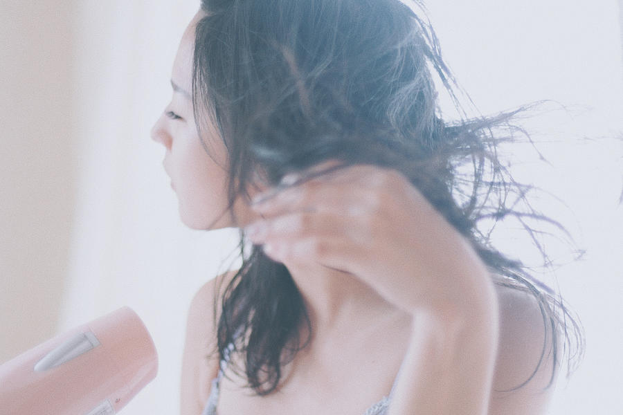 Woman drying her hair with a hair dryer at home Photograph by Yue_