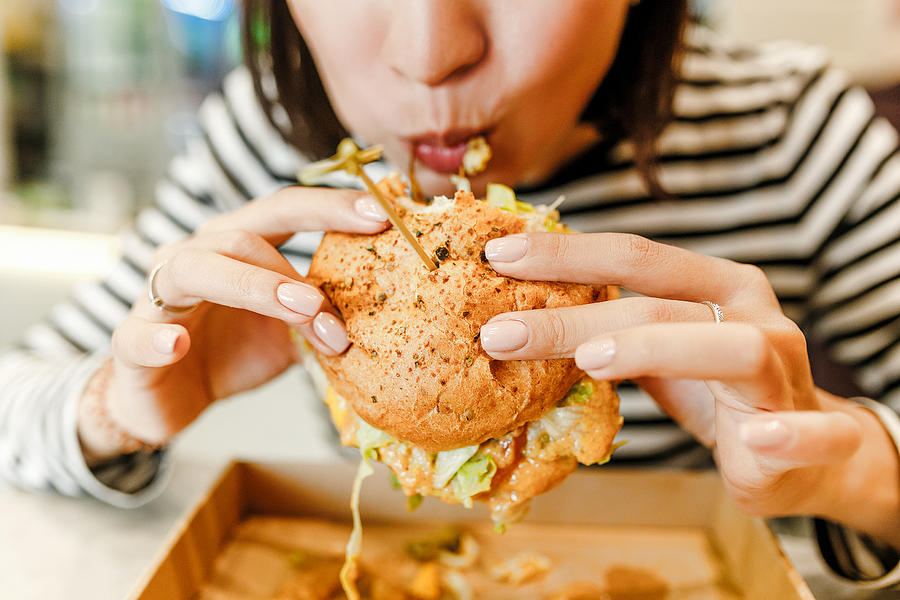 Woman eating a hamburger in modern fastfood cafe, lunch concept Photograph by Frantic00