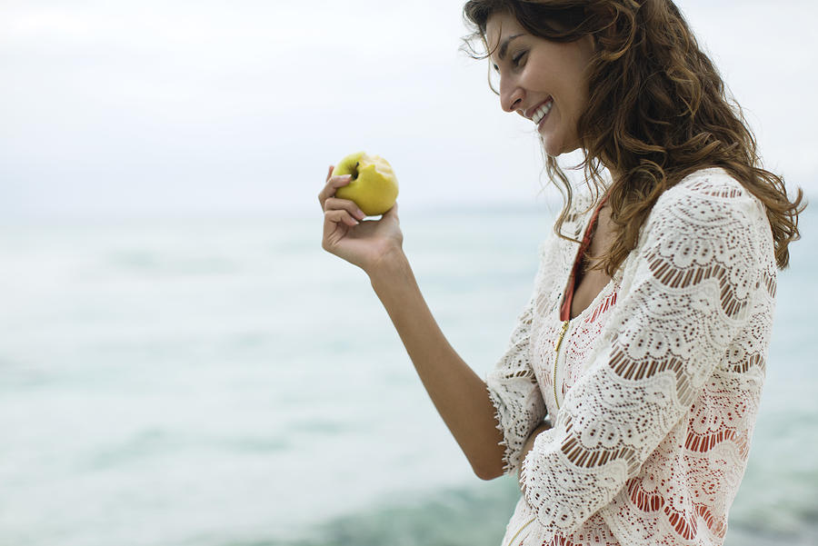 Woman eating apple at the beach Photograph by PhotoAlto/Antoine Arraou