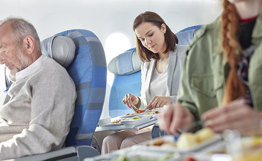 Woman eating dinner on airplane Photograph by Caia Image