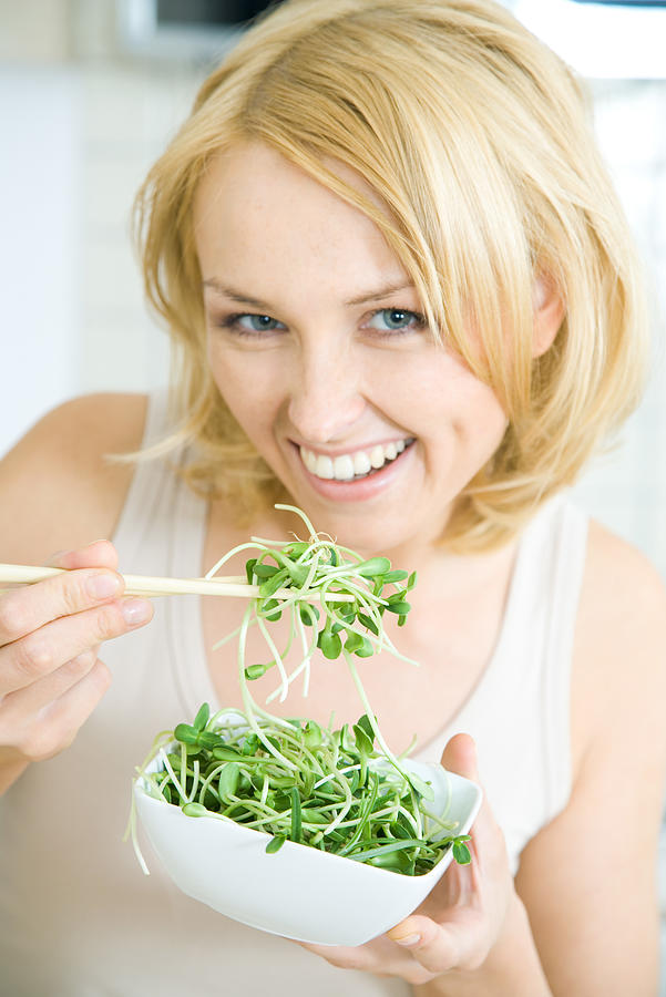 Woman eating radish sprouts with chopsticks, smiling at camera Photograph by PhotoAlto/Rafal Strzechowski