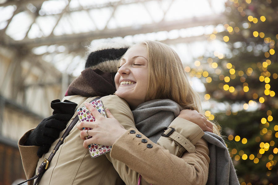 Woman embraces her friend at railroad station, christmas tree in background. Photograph by Betsie Van der Meer