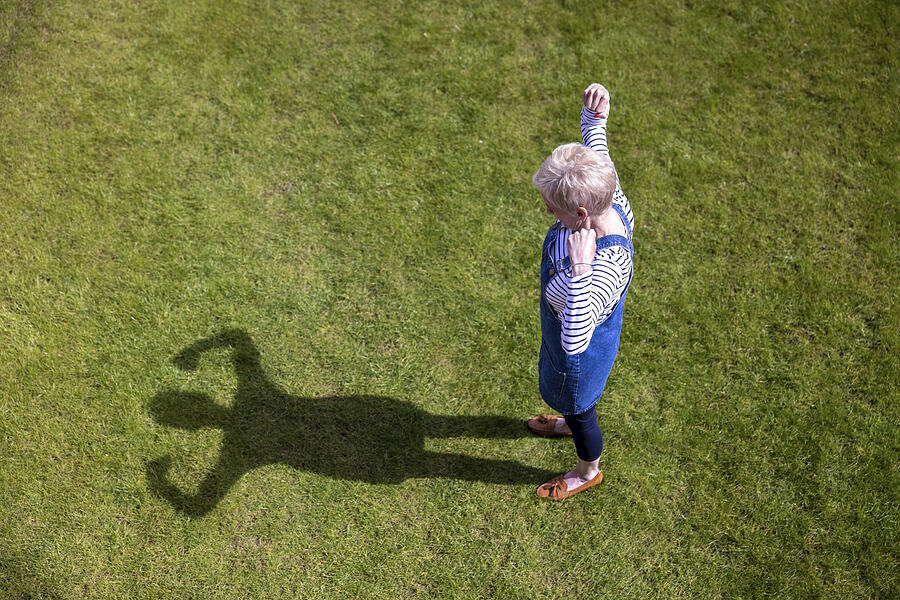 Woman flexing muscles while looking at shadow on grass Photograph by Westend61