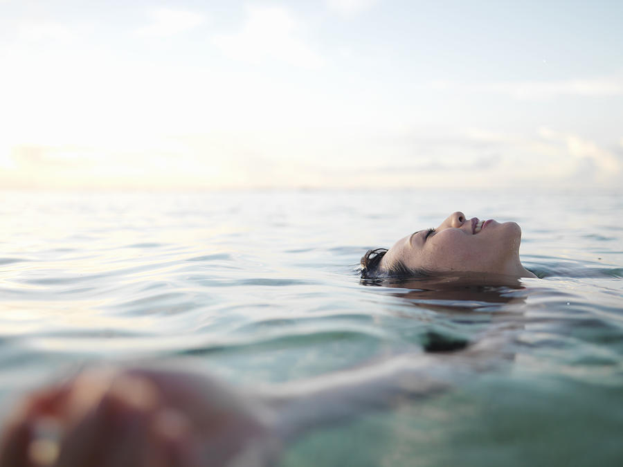 Woman floating in sea, smiling, profile Photograph by Michael H