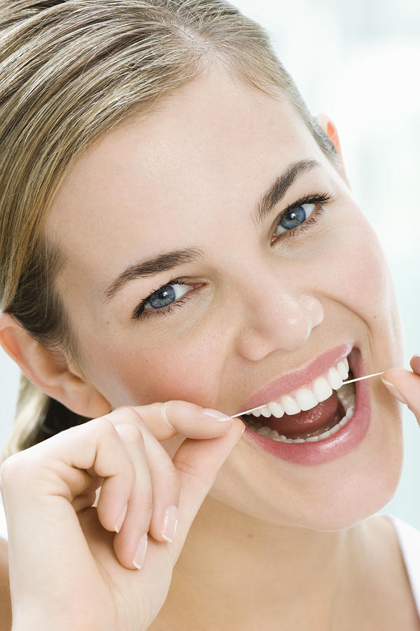 Woman flossing her teeth, smiling, close-up Photograph by Pando Hall