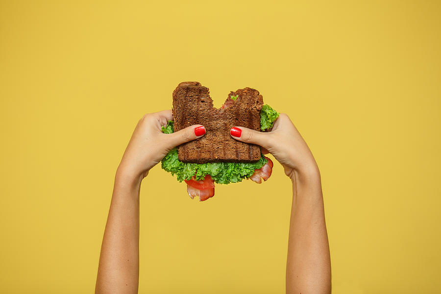 woman hands hold bitten sandwich on yellow background. Sandwich promotion concept. Photograph by Kateryna Kukota