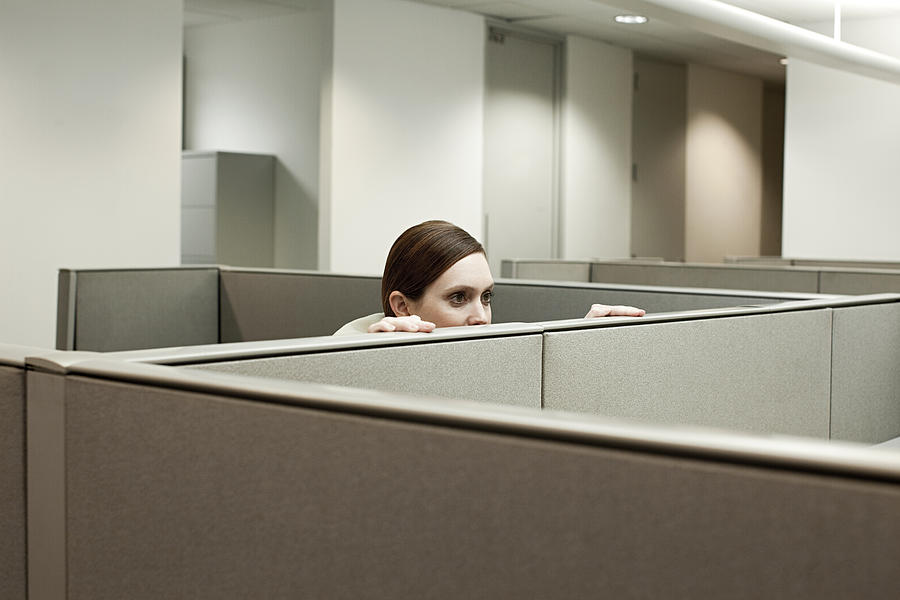 Woman hiding behind cubicle in office Photograph by Image Source