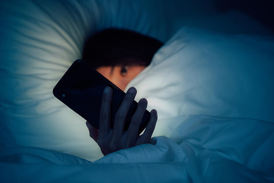 Woman hiding under the blanketed and using smart phone at late night on bed Photograph by Oscar Wong