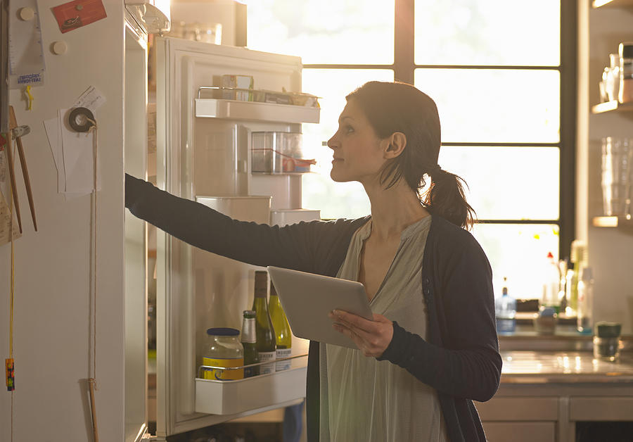 Woman holding an iPad whilst looking in the fridge Photograph by 10000 Hours