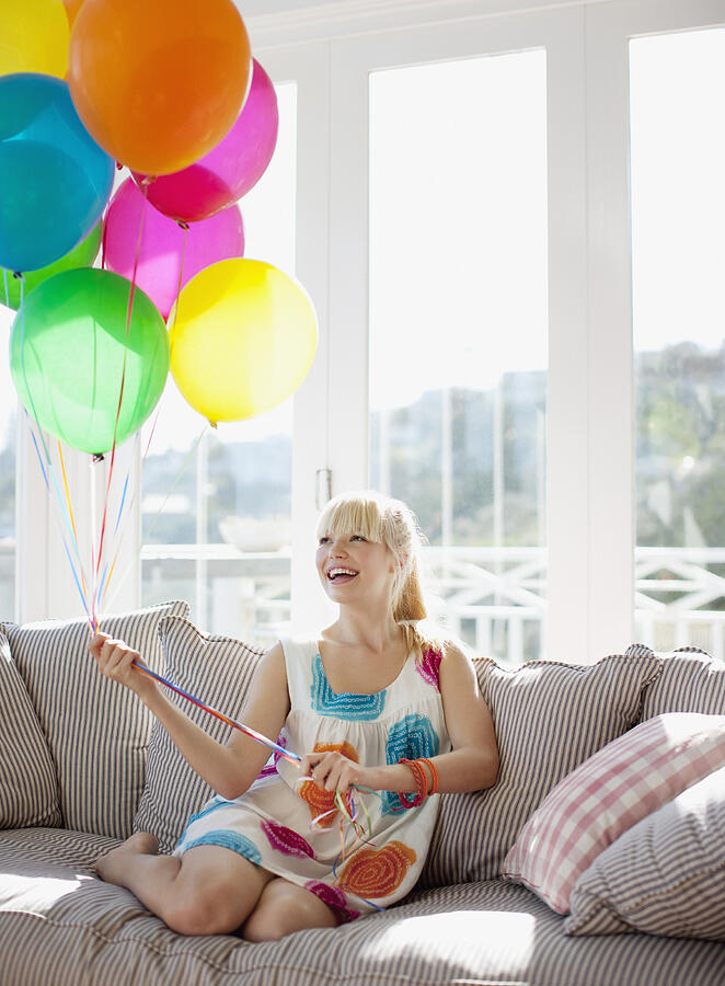 Woman holding balloons on sofa in living room Photograph by Paul Bradbury