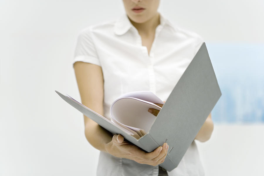 Woman holding binder, reading document, cropped view Photograph by PhotoAlto/Alix Minde