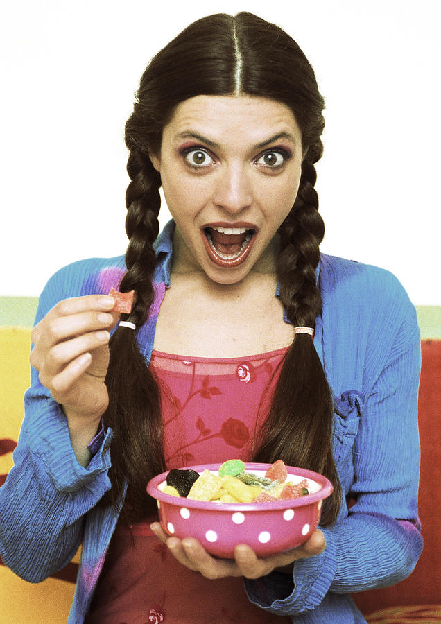 Woman holding bowl of candy, mouth wide open, portrait. Photograph by Corinne Malet