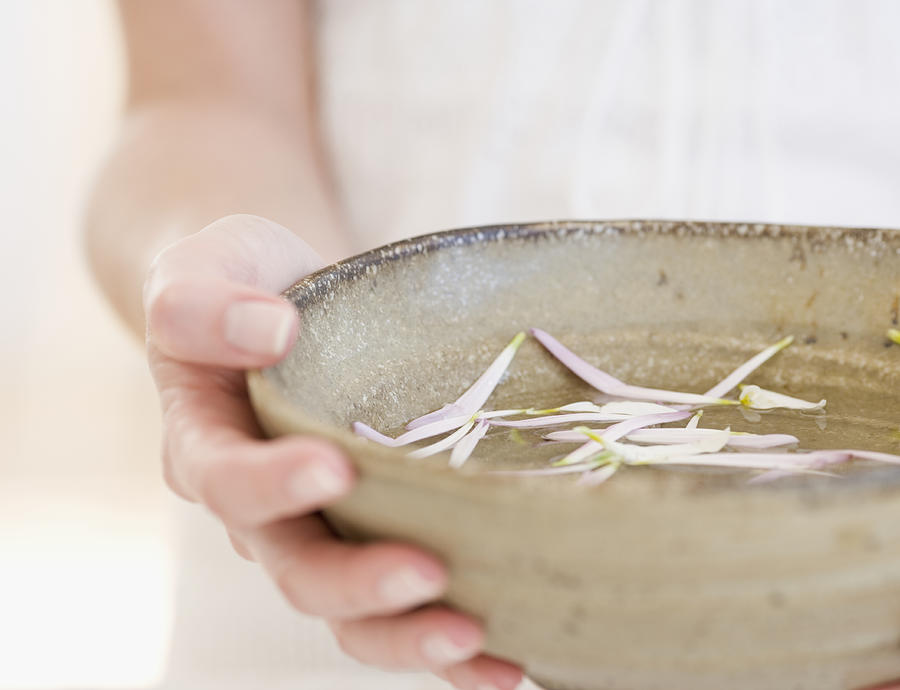 Woman holding bowl of petals in water, close-up, mid section Photograph by Jamie Grill