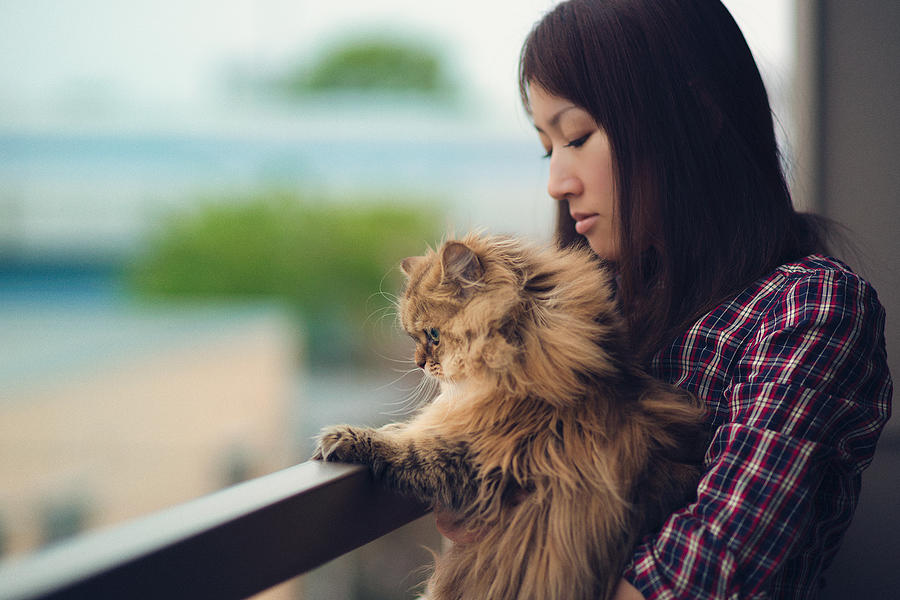 Woman holding cat on apartment balcony Photograph by Benjamin Torode