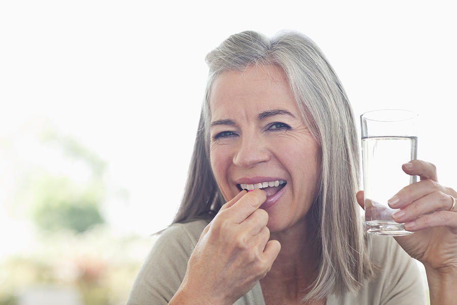 Woman holding glass of water taking pill Photograph by Sam Edwards