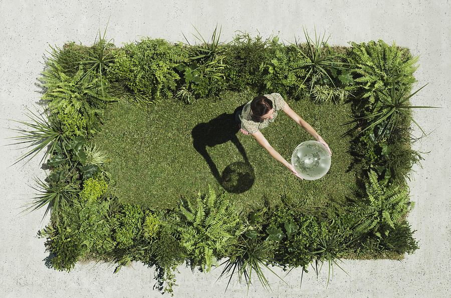 Woman holding globe on lush lawn in cement courtyard Photograph by Martin Barraud