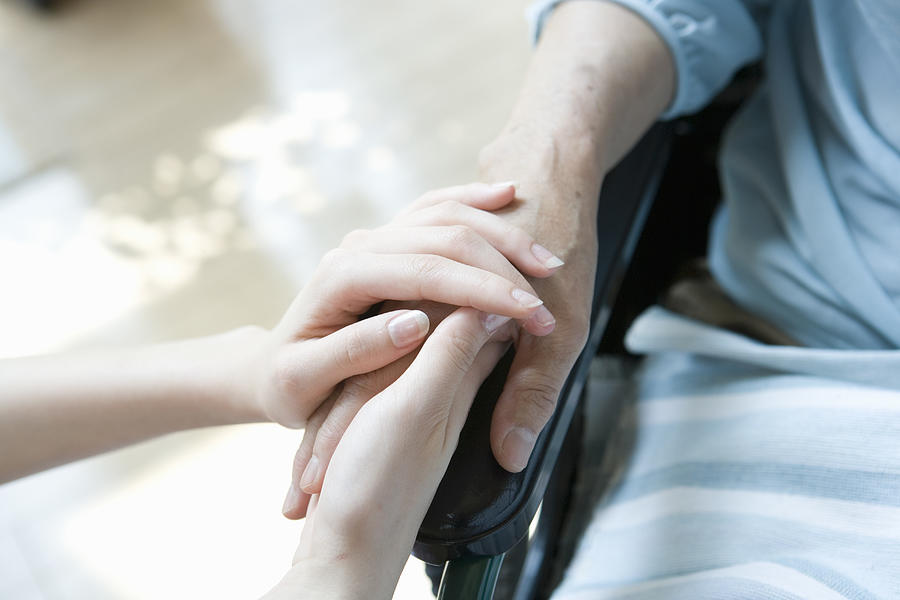 Woman holding hands of patient in wheelchair Photograph by Indeed
