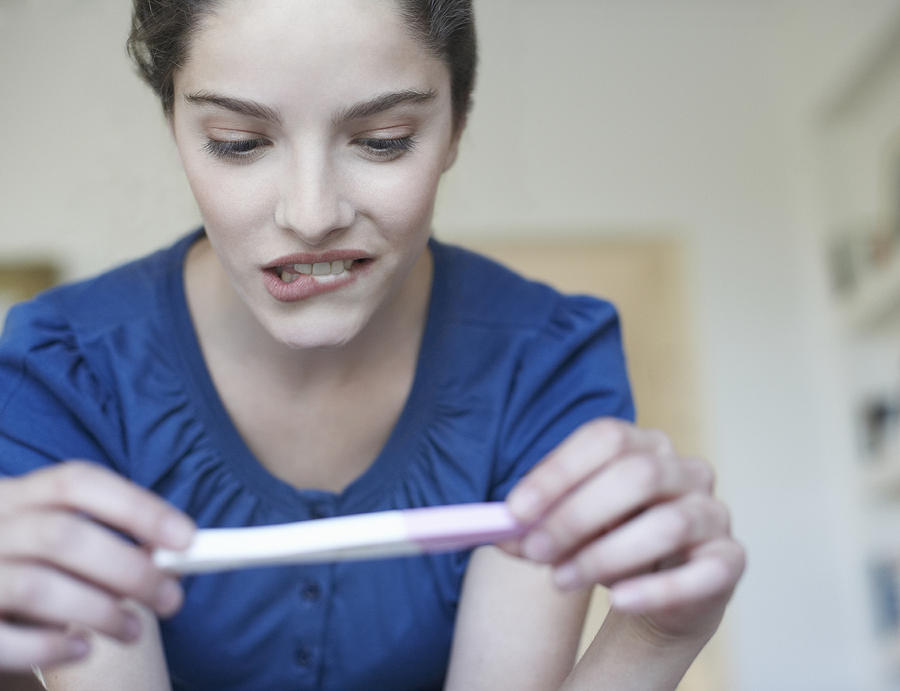 Woman holding home pregnancy test and looking worried Photograph by Sam Edwards