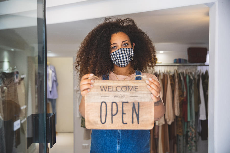 Woman holding Open sign in a small business boutique shop after Covid-19 pandemic Photograph by LeoPatrizi