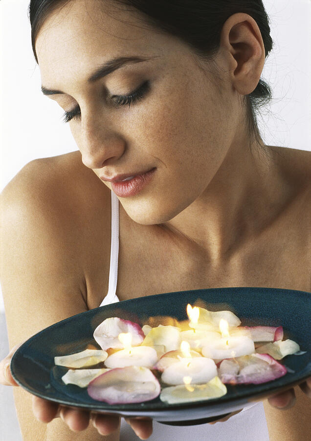 Woman holding plate of candles and rose petals, looking down, close-up Photograph by Frederic Cirou