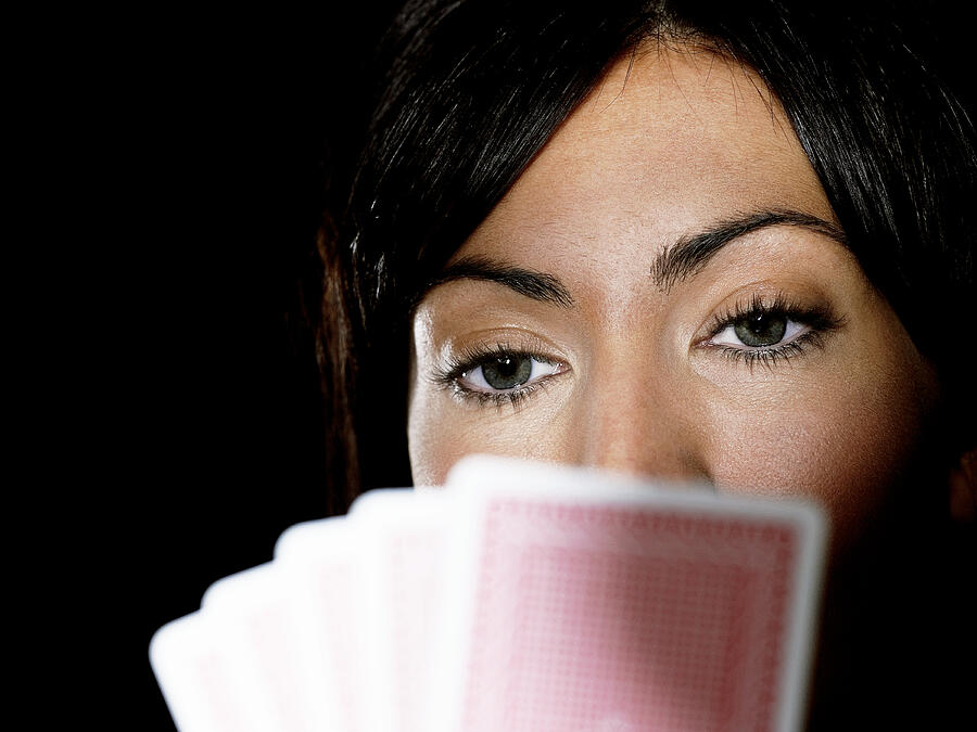 Woman holding playing cards up to face, close-up (focus on woman) Photograph by John Howard