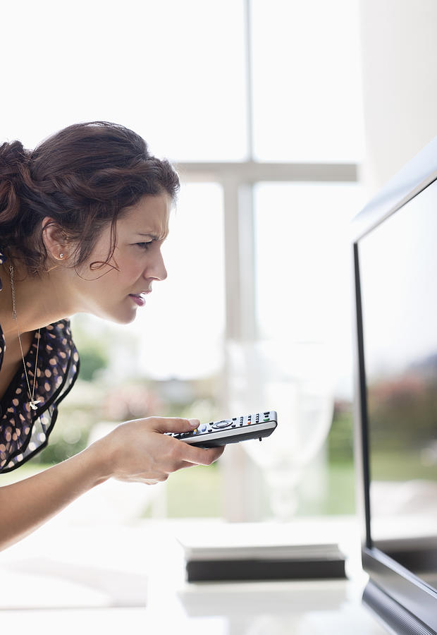 Woman holding remote control to TV and squinting Photograph by Paul Bradbury