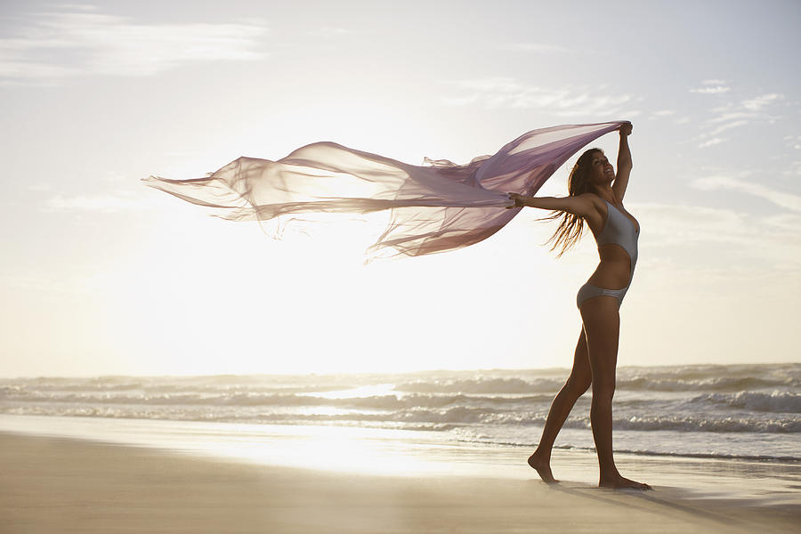 Woman holding sarong overhead on beach Photograph by Tom Merton