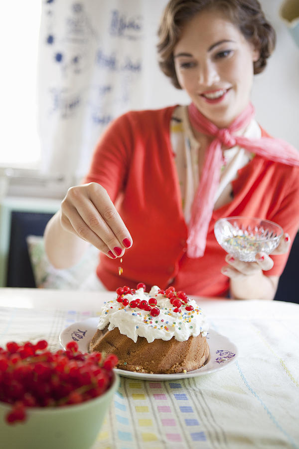 Woman icing a cake in kitchen Photograph by Photo_Concepts