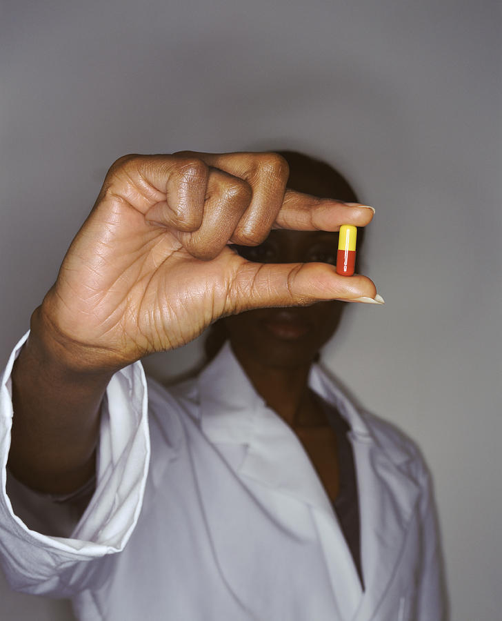 Woman in a Lab Coat Holds Out a Pill Between Her Fingers Photograph by Noel Hendrickson