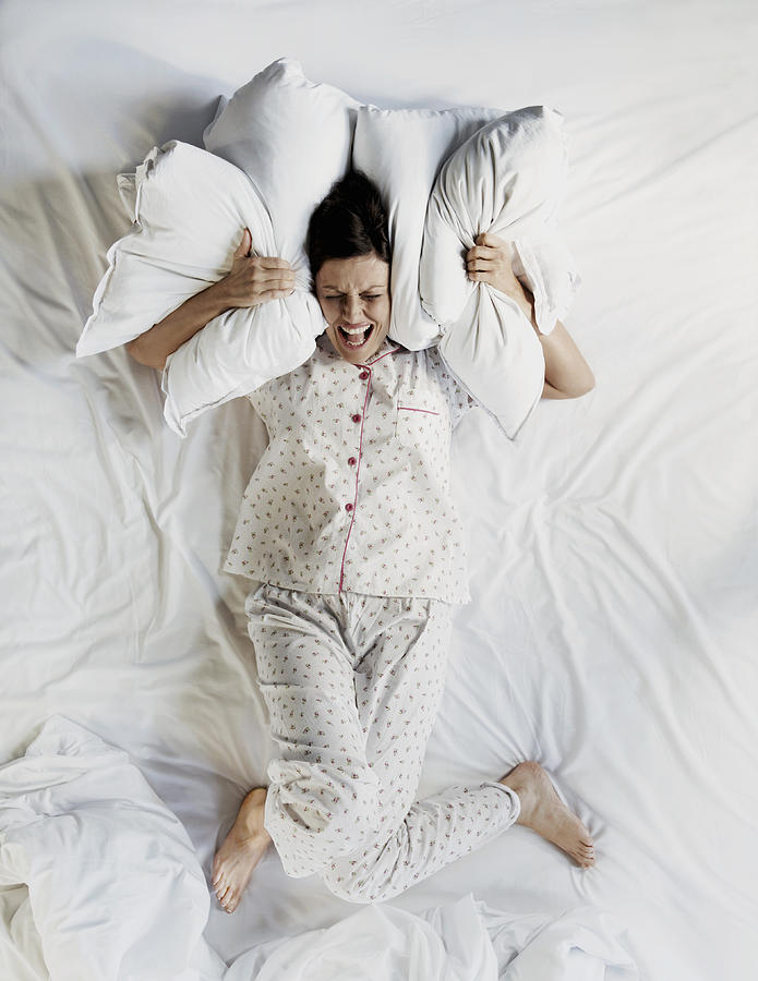 Woman in bed using pillows to cover her ears Photograph by Flashpop